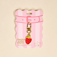 The Darling Effect’s Strawberry Pawfect Collar Charm features a gold lobster clasp and red strawberry with yellow leaves, displayed on a pink, wavy-edged card with stripes and “Pawfect Collar Charm” text—perfect for any pet collar.