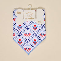 The Darling Effect’s Bow-Wow Pet Bandana-All-American Darling is a white cotton bandana with a blue edge, featuring American flags, red flowers, and blue stars. Displayed on a hanger in size L/XL.