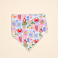 The Darling Effect Bow-Wow Pet Bandana-Ciao Bella is a vibrant cotton accessory with crabs, flowers, lemons, cherries, and shells on a light blue and white background—ideal for stylish pet fashion lovers.
