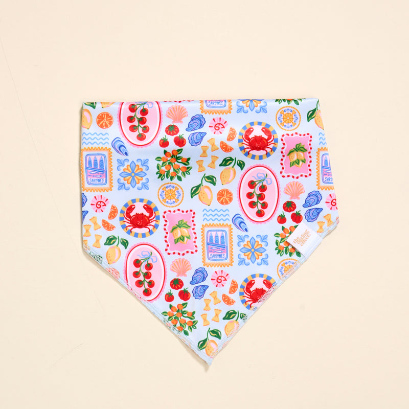 The Darling Effect Bow-Wow Pet Bandana-Ciao Bella is a vibrant cotton accessory with crabs, flowers, lemons, cherries, and shells on a light blue and white background—ideal for stylish pet fashion lovers.