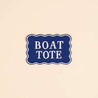 Add colorful flair to your collection with The Darling Effect’s Boat Tote Mix & Match Iron-On Patch—a blue rectangular patch with wavy edges, white border, and bold uppercase “BOAT TOTE”—perfect for personalizing bags or jackets.