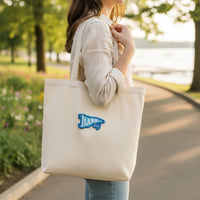 A woman stands outside on a sunny day with The Darling Effect’s Lake Day Mix & Match Iron-On Patch on her beige tote. She wears a light shirt and jeans—ideal for fans of customizing jackets or adding colorful patches.