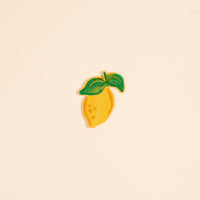The Lemon Mix & Match Iron-On Patch by The Darling Effect features an embroidered yellow lemon with two green leaves on a light beige background—ideal for adding a pop of color and style to your clothes.