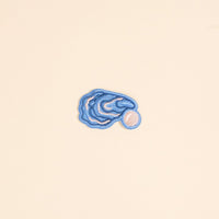The Darling Effect’s Oyster Mix & Match Iron-On Patch features a blue oyster with a pearl on a beige background—perfect for customizing your style with its colorful, easy-to-apply embroidered design.