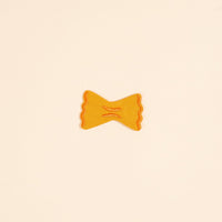 A yellow-orange farfalle pasta is centered on a plain beige background, resembling The Darling Effect's Pasta Mix & Match Iron-On Patch—a playful nod to colorful iron-on patch designs.