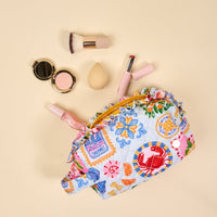 The Darling Effect's Ciao Bella Essentials Quilted Cosmetic Pouch, shown open on a beige surface with brushes, compact, sponge, lipstick, and lip gloss in pink or neutral tones—ideal for organizing your beauty essentials on the go.