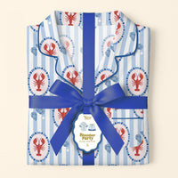 The Darling Effect's Harbor House Slumber Party Pajama Shorts Set, featuring folded blue-and-white stripes with red lobsters, is tied with a ribbon and a tag reading “Slumber Party Pajama Set S,” arranged on a cream background.