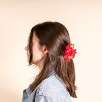 A woman with shoulder-length brown hair wears a denim jacket and sports a cute hairstyle secured with The Darling Effect's Strawberry Patch Shape Up Claw Clip against a plain light beige background.