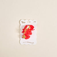 The Darling Effect’s Strawberry Patch Shape Up Claw Clip, a red strawberry-shaped accessory, is shown on white packaging with a cream background—perfect for adding a cute touch to any hairstyle.