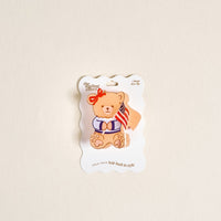 Add a touch of charm with The Darling Effect’s Star Spangled Bear Shape Up Claw Clip—a cute teddy bear in a blue and white striped shirt with a red bow, sitting atop an American flag-themed accessory.