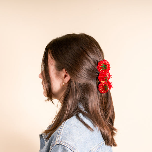 A young person with dark brown hair styled cutely, wearing The Darling Effect's Tomatoes Shape Up Claw Clip as a hair accessory, paired with a denim jacket and a gold hoop earring.