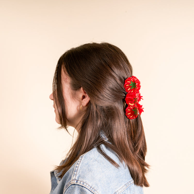 A young person with dark brown hair styled cutely, wearing The Darling Effect's Tomatoes Shape Up Claw Clip as a hair accessory, paired with a denim jacket and a gold hoop earring.