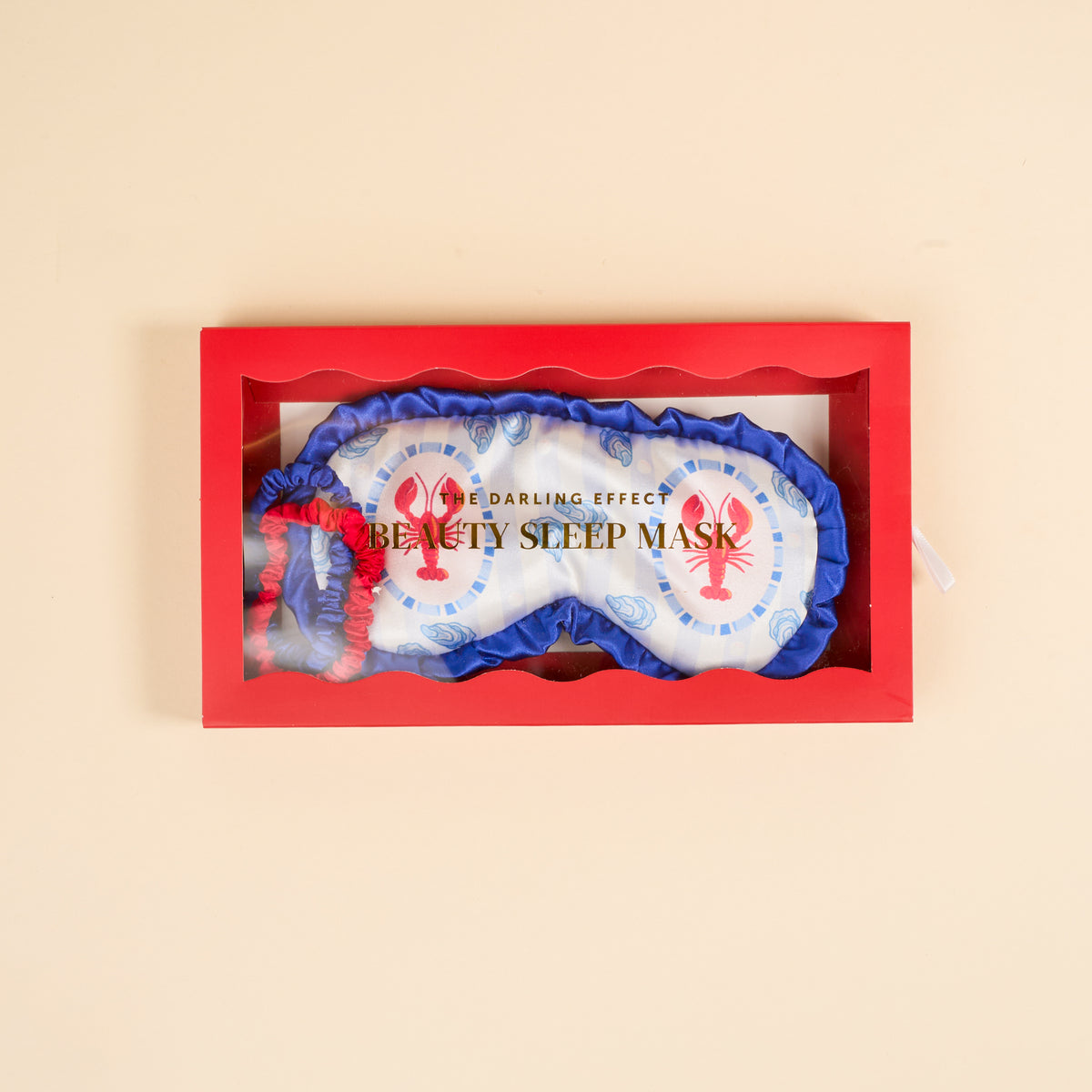 The Darling Effect Harbor House Beauty Sleep Mask features white satin with blue trim, red lobster designs, and "BEAUTY SLEEP MASK" text. It has a matching red and blue elastic strap and comes in a red box with a clear window.