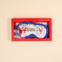 The Darling Effect Harbor House Beauty Sleep Mask features white satin with blue trim, red lobster designs, and "BEAUTY SLEEP MASK" text. It has a matching red and blue elastic strap and comes in a red box with a clear window.