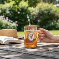 A hand holds The Darling Effect’s Lobster Square Glass Cup filled with iced tea, lemon slices, and a straw. An open book and straw hat sit on an outdoor wooden table with greenery in the background.