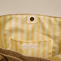 Close-up of the Sea, Sand, Sun Straw & Sun Tote by The Darling Effect, featuring a yellow and white striped lining, inner pocket with branded label, and magnetic snap—spacious enough for your next vacation.