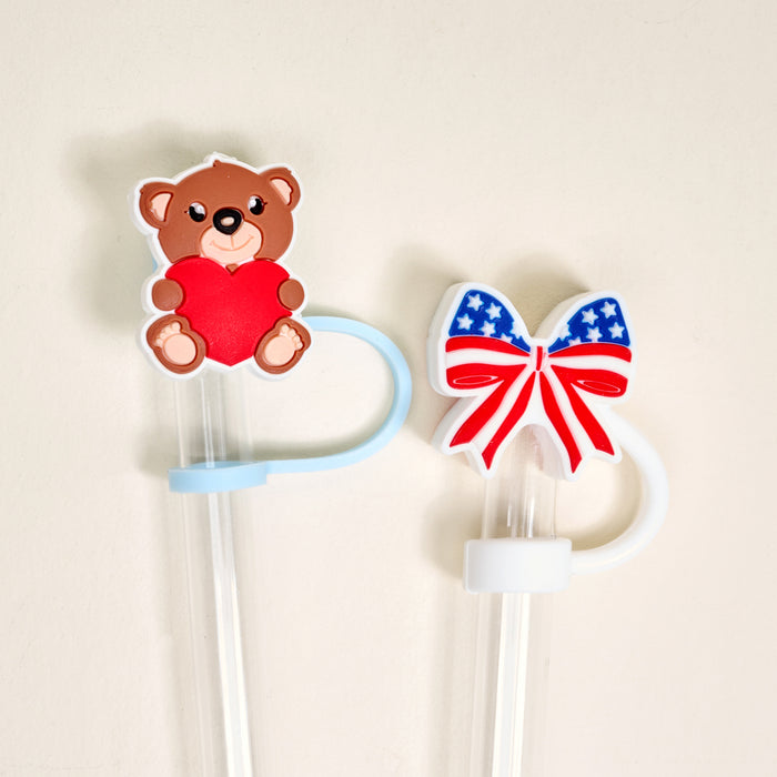 The Darling Effect’s Star Spangled Bear Straw Topper Set includes two reusable straws with leak-resistant toppers: a teddy bear holding a red heart and a bow in American flag colors—both fun, practical accessories against a plain background.