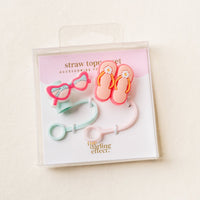 The Darling Effect's Sunny Style Straw Topper Set features colorful silicone toppers shaped like pink sunglasses and flip-flops, packaged in a clear box—fun, leak-resistant drinkware accessories for your beverages.