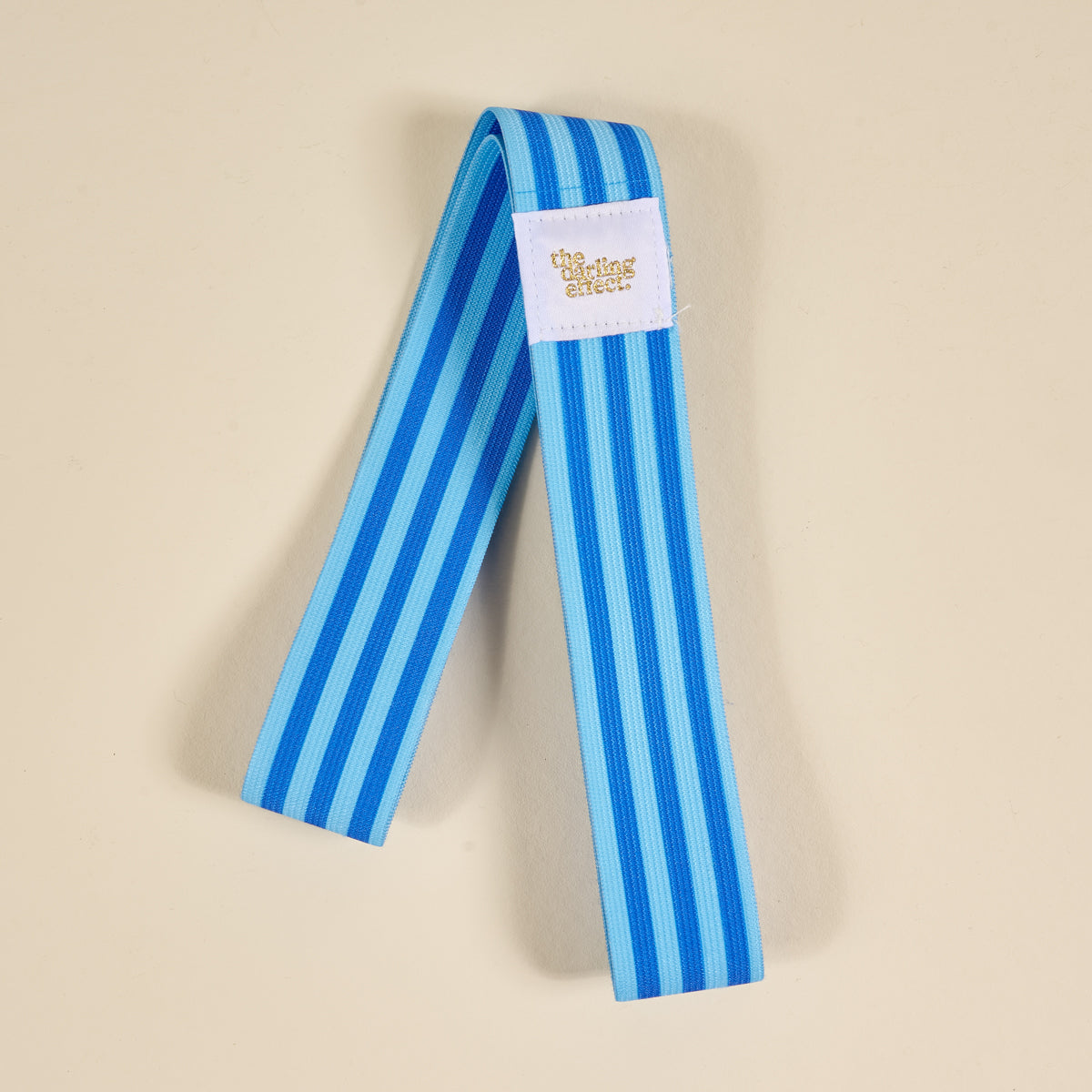 A blue and light blue striped Put Towel Band-Stripes Blue Stay by The Darling Effect, featuring a white label with “the charting circle,” lies on a beige surface.