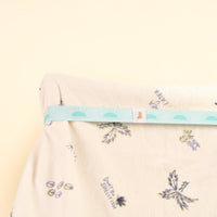 A soft white fabric with blue and yellow plant and fruit illustrations is partially wrapped in the-darling-effect's Put Towel Band-Sunshine Aqua Stay, featuring a light blue sunburst pattern, all set against a light beige background.