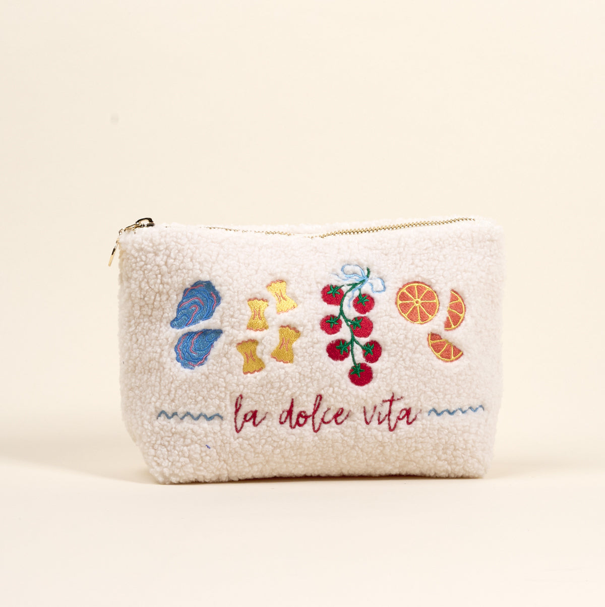 The Darling Effect La Dolce Vita Teddy Pouch is a cream sherpa zip pouch with embroidered mushrooms, pasta, tomatoes, and orange slices above “la dolce vita” in red script.