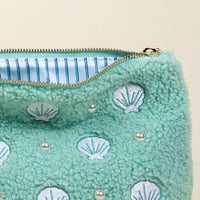 The-darling-effect’s Seashells & Pearls Teddy Pouch features soft mint green sherpa, embroidered white seashells, pearl-like beads, a zip closure, and a partially open blue and white striped lining.