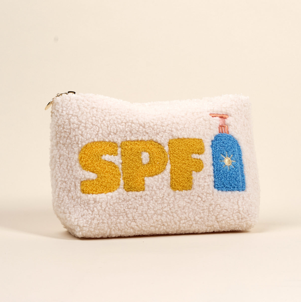 A white sherpa pouch with the letters SPF in yellow and a blue sunscreen bottle with a flower design, embroidered on the front.