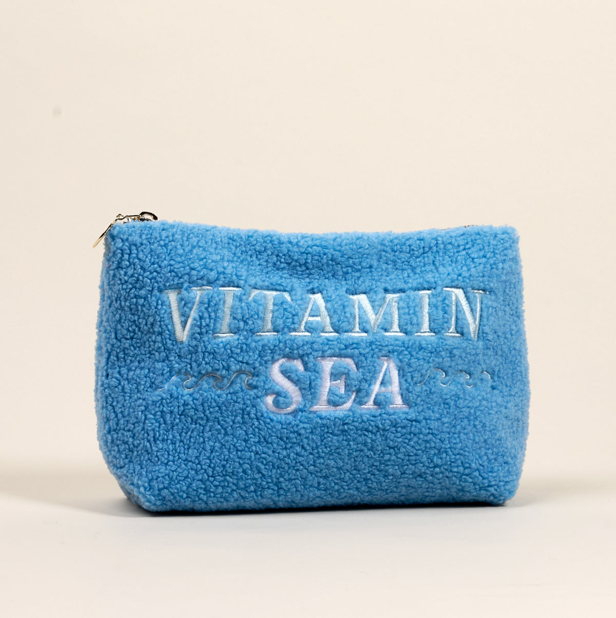 The Darling Effect Vitamin Sea Teddy Pouch features blue fluffy sherpa fabric with "Vitamin Sea" and wave details embroidered in white, making it a stylish accessory.