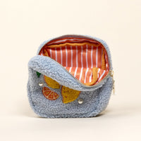 The Square Citrus & Pearls Teddy Pouch by The Darling Effect is a small, fuzzy light blue pouch made from cozy sherpa fabric with a zipper, featuring embroidered lemon and orange slices on the front. It sits open to reveal a pink and white striped fabric lining.