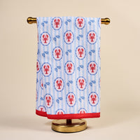 The Darling Effect’s Harbor House Waffle Tea Towel, featuring red lobsters and blue shells with vertical stripes and a red border, brings coastal charm and absorbency to your kitchen decor.