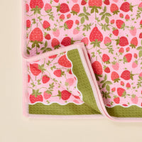 The Strawberry Fields Waffle Tea Towel by The Darling Effect features a pink strawberry and green leaf pattern, scalloped border, pink edging, and a green underside—adding decorative charm to your space.
