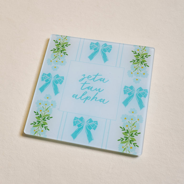 The Darling Effect’s Zeta Tau Alpha Acrylic Coaster features a light blue background with blue bows, green florals, and “zeta tau alpha” in cursive—perfect for showcasing your sorority pride or gifting to a fellow sister.