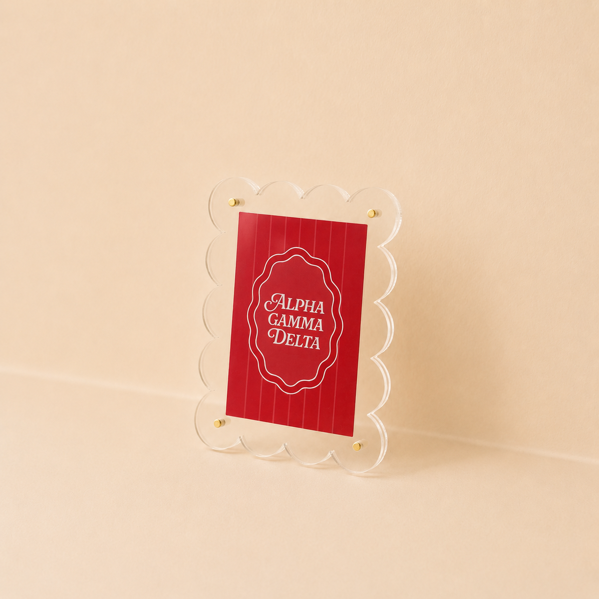 The Darling Effect's Alpha Gamma Delta Mini Acrylic Picture Frame Magnet features a clear scalloped acrylic frame displaying a red card with “ALPHA GAMMA DELTA” in white, styled like a polaroid and perfect for any surface.