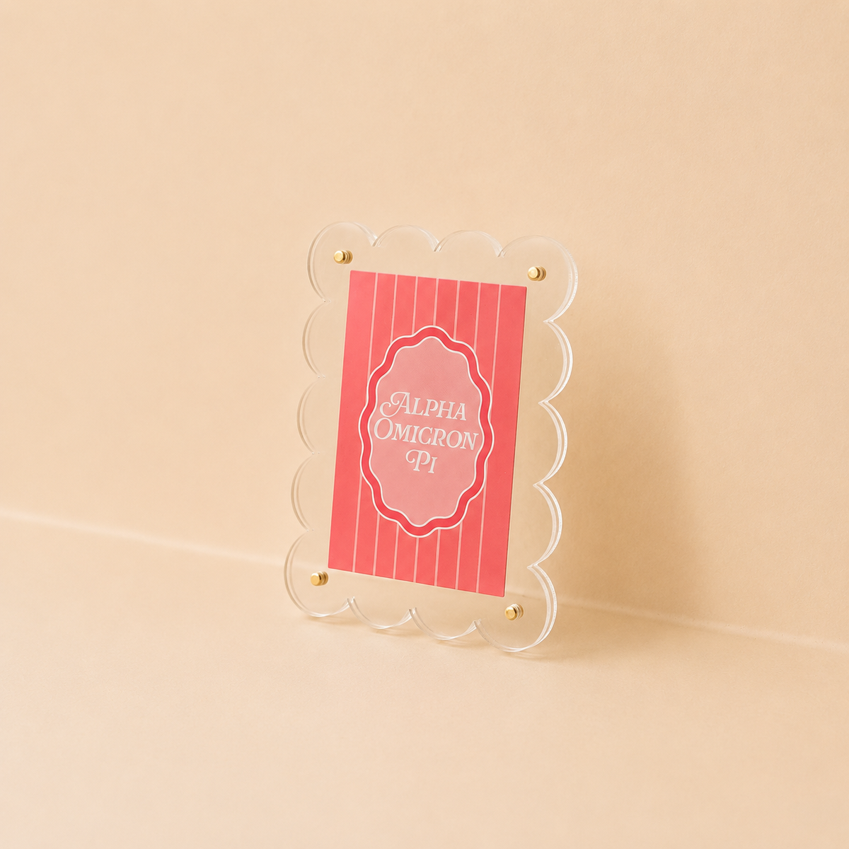 The Darling Effect's Alpha Omicron Pi Mini Acrylic Picture Frame Magnet features a clear scalloped edge and gold screws, displaying a red Alpha Omicron Pi card—ideal for showcasing small prints or polaroid magnets.