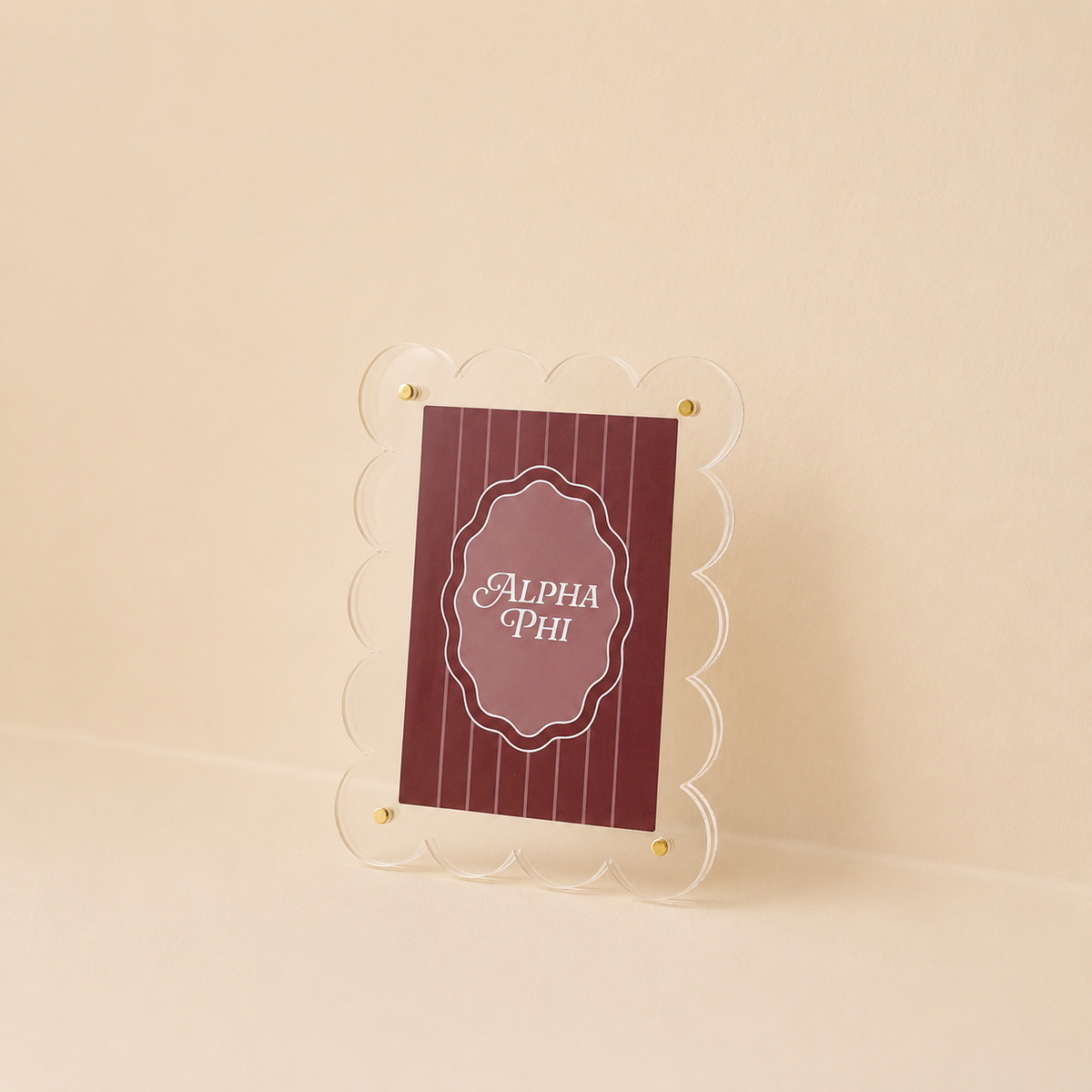 The Darling Effect's Alpha Phi Mini Acrylic Picture Frame Magnet features a clear, scalloped edge and displays a maroon card with thin vertical lines and "Alpha Phi" in white script on a beige background.
