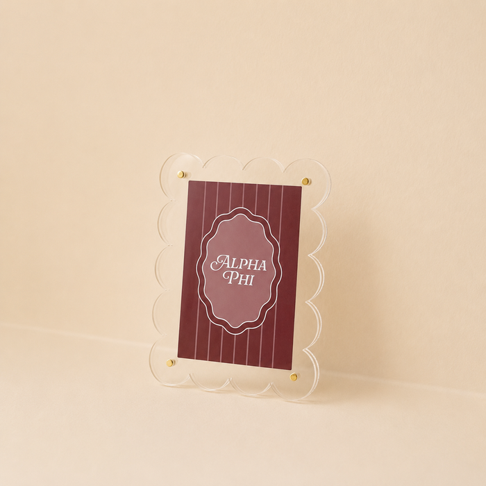 The Darling Effect's Alpha Phi Mini Acrylic Picture Frame Magnet features a clear, scalloped edge and displays a maroon card with thin vertical lines and "Alpha Phi" in white script on a beige background.