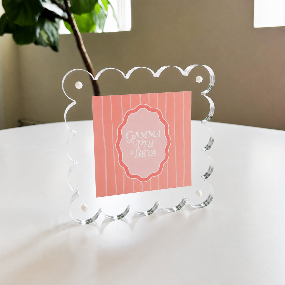 The Darling Effect’s Gamma Phi Beta Square Scalloped Acrylic Frame showcases a pink, vertically striped “Gamma Phi Beta” card in white script—a chic, modern accent for your space.