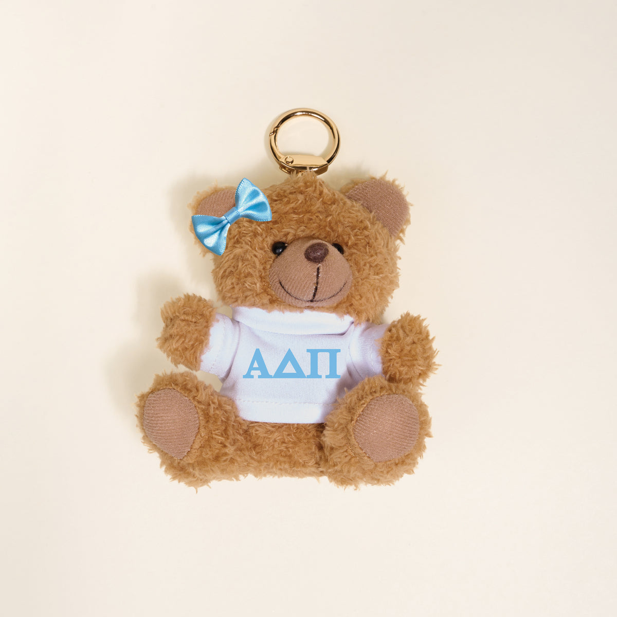 The Darling Effect's Alpha Delta Pi Teddy Bear Bag Charm is a small brown bear keychain with a blue bow and white shirt featuring blue ΑΔΠ Greek letters—perfect as a Bid Day gift or cute accessory.