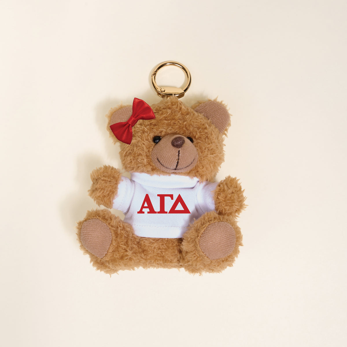 The Darling Effect’s Alpha Gamma Delta Teddy Bear Bag Charm features a small brown bear keychain with a red bow and a white shirt displaying red Greek letters—perfect as a unique sorority gift or cute bag accessory.