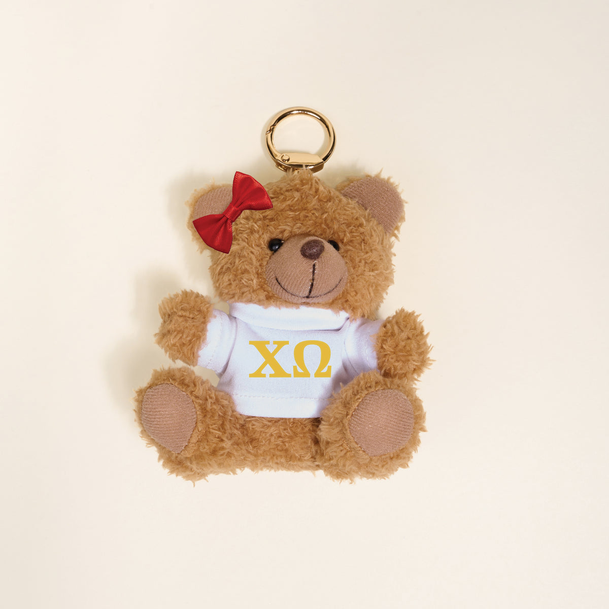 The Darling Effect Chi Omega Teddy Bear Bag Charm features a cute mini bear with a red bow and white shirt with yellow ΧΩ Greek letters—perfect as a sorority gift or bag charm. Displayed on a simple light background.