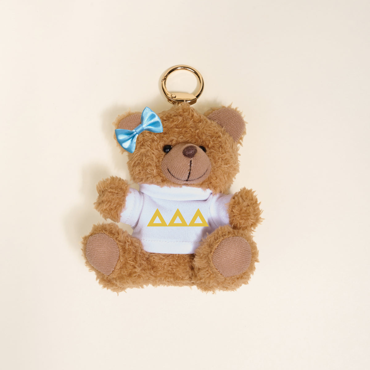 The Darling Effect Delta Delta Delta Teddy Bear Bag Charm is a small plush bear keychain with a blue bow on its right ear and a white shirt with three yellow triangles, perfect as a cute sorority accessory or bag charm on any light background.