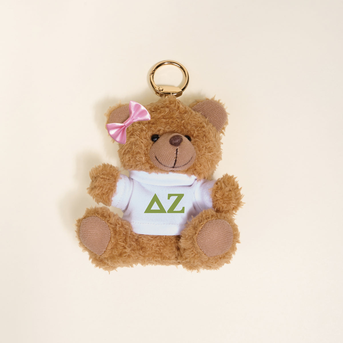 The Darling Effect’s Delta Zeta Teddy Bear Bag Charm features a small brown bear with a pink bow, wearing a white shirt with green ΔΖ letters—perfect as a Bid Day gift or cute accessory for your bag.