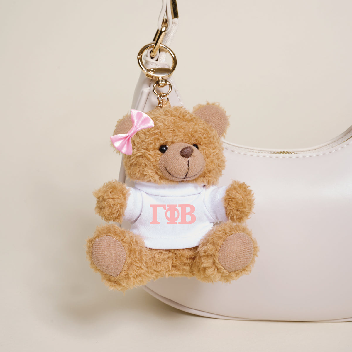The Darling Effect's Gamma Phi Beta Teddy Bear Bag Charm is a small brown teddy bear keychain with a pink bow and white shirt with Greek letters, perfect as a cute sorority accessory or to hang on your favorite bag.