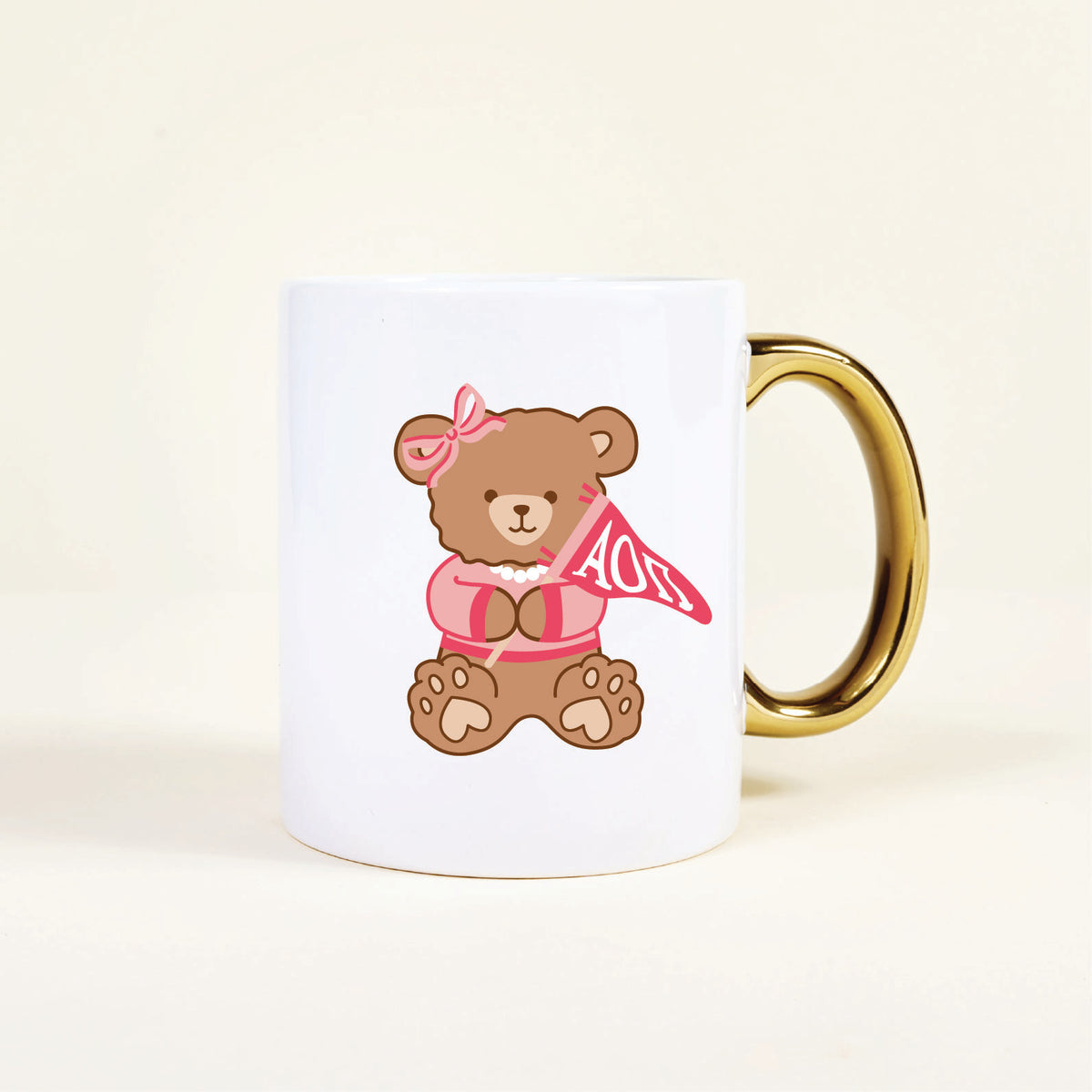 Enjoy your morning coffee or tea with The Darling Effect Alpha Omicron Pi 11 oz Cozy Cute Ceramic Mug, featuring a sweet bear in a pink bow and shirt holding an “AOII” pennant and accented with a gold handle—perfect for any sorority member.