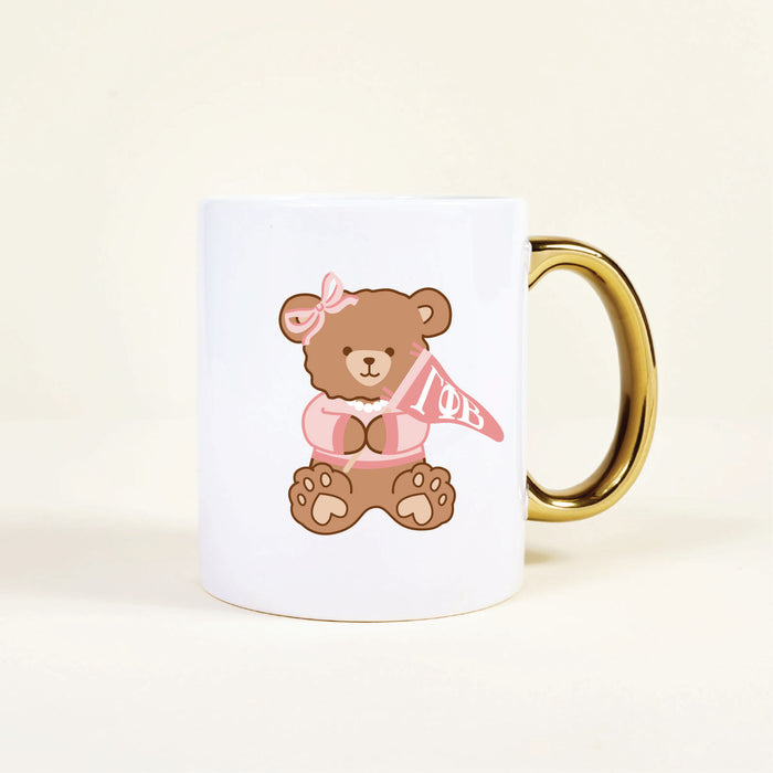 Enjoy your morning coffee with The Darling Effect's Gamma Phi Beta 11 oz Cozy Cute Ceramic Mug, featuring a brown teddy bear in a pink sweater holding a Gamma Phi Beta pennant—perfect for sorority members or as an adorable gift.