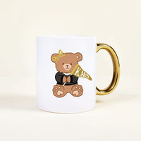 The Darling Effect’s Kappa Alpha Theta 11 oz Cozy Cute Ceramic Mug features a charming teddy bear in a black top, pearl necklace, yellow bow, and gold handle, holding a yellow KAO flag—perfect for sorority members.