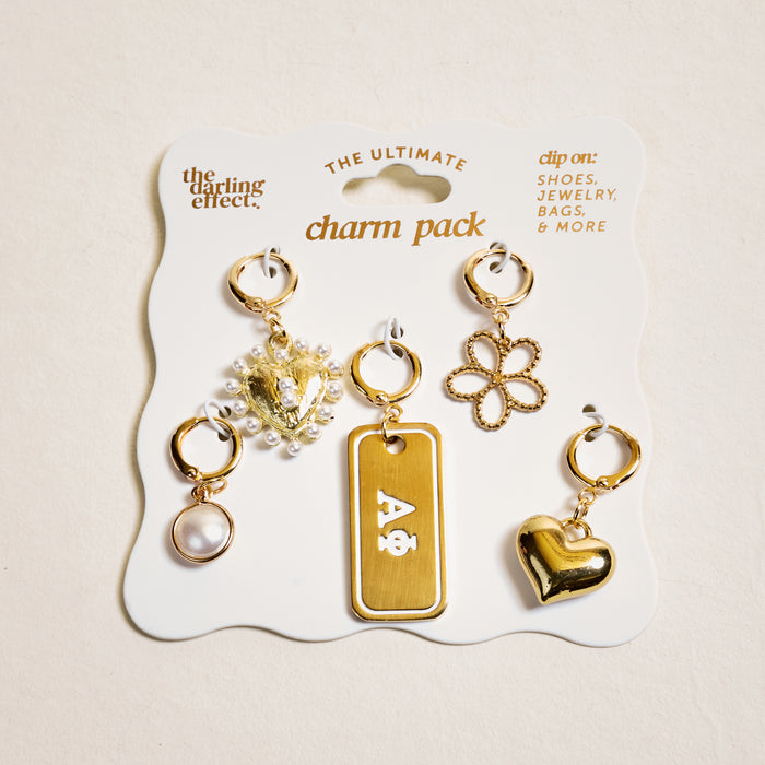 Alpha Phi The Ultimate Charm Pack by The Darling Effect features five gold charms—a pearl, a pearl heart, a Greek letter tag, a flower outline, and a shiny gold heart—displayed on a white card. Perfect sorority jewelry!.
