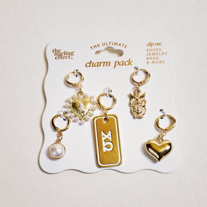 Chi Omega The Ultimate Charm Pack by The Darling Effect includes five gold-tone charms—a pearl, jeweled heart, XO tag, owl, and shiny heart—on a white card to clip onto shoes, jewelry, bags, or necklaces for extra sorority style.