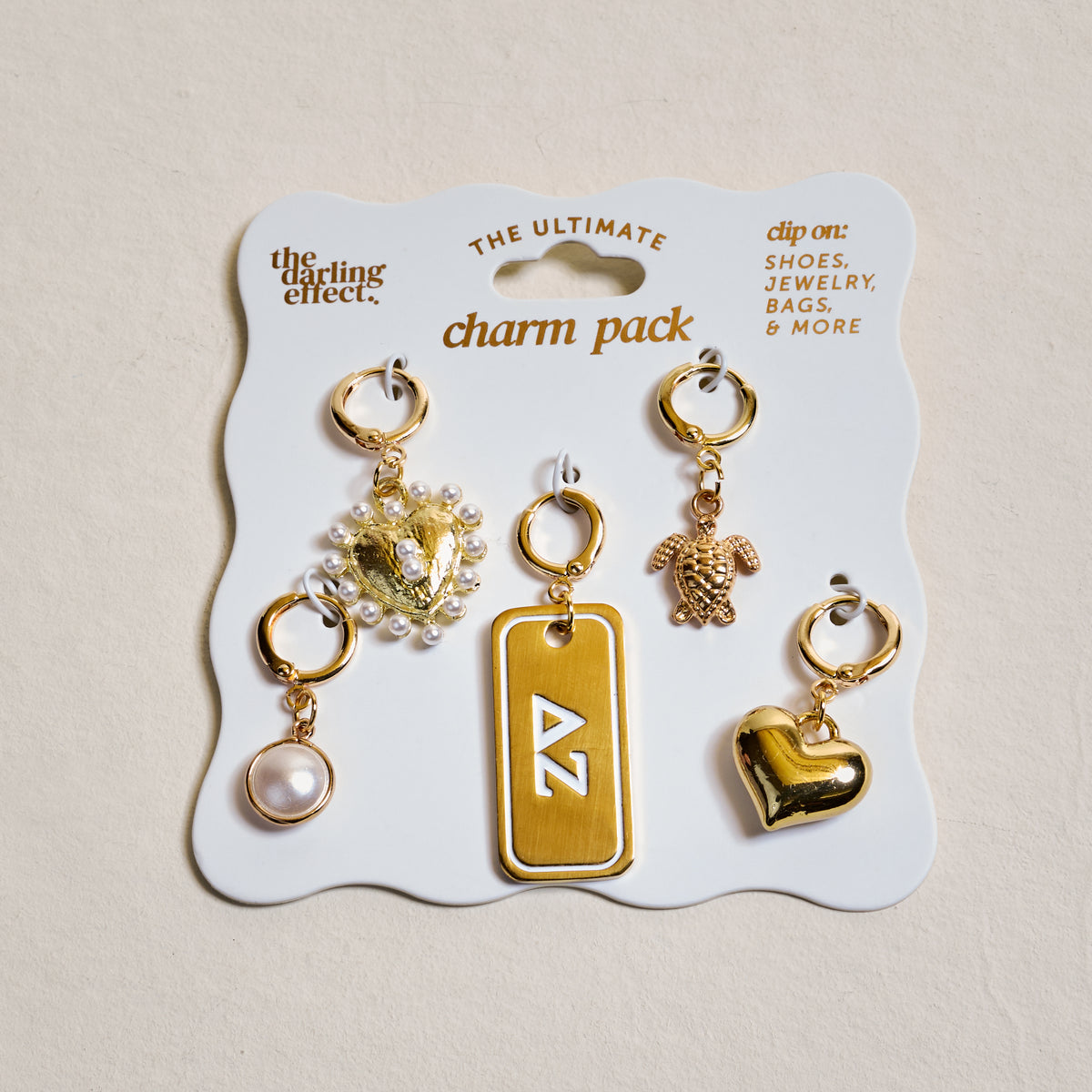 The Darling Effect’s Delta Zeta The Ultimate Charm Pack features six gold charms—a pearl, crystal flower, ΔZ rectangle tag, teddy bear, heart, and pearl hoop—perfect for clipping to scrunchie charm sets or other accessories.