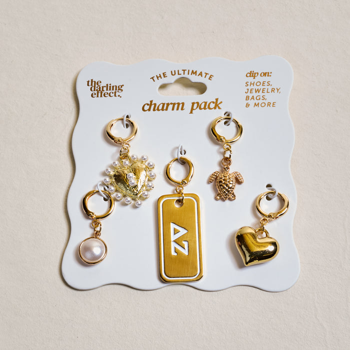 The Darling Effect’s Delta Zeta The Ultimate Charm Pack features six gold charms—a pearl, crystal flower, ΔZ rectangle tag, teddy bear, heart, and pearl hoop—perfect for clipping to scrunchie charm sets or other accessories.